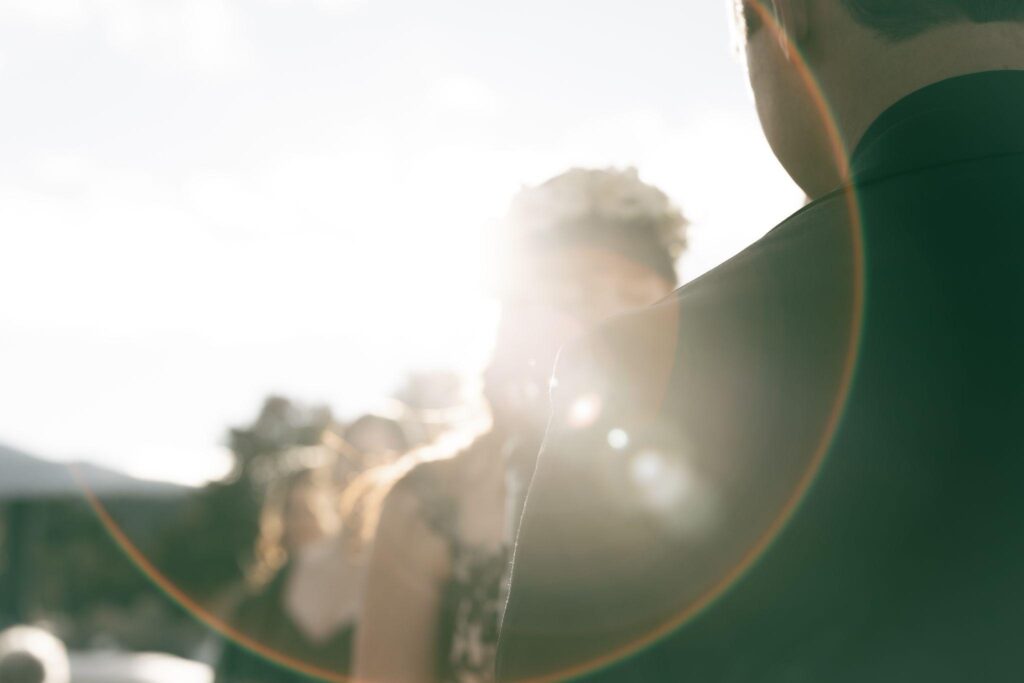 Sunlit guests seen past a man's shoulder with a soft lens flare