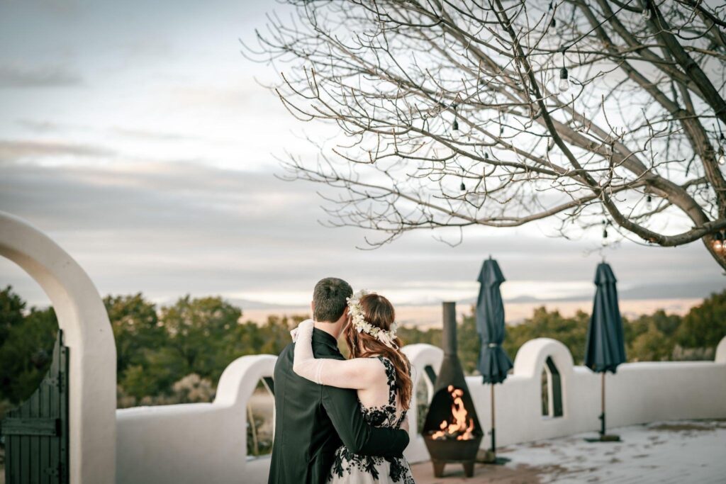 Bride and groom embrace on an adobe patio beside a fire pit