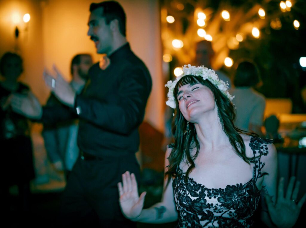 Bride in a flower crown dances with eyes closed under string lights